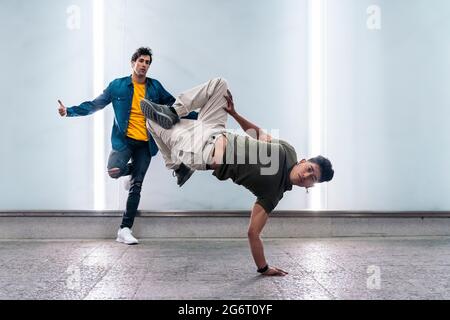 Two multi-ethnic friends dancing break dance and having fun against white wall with lights. Stock Photo