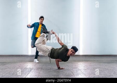 Amazing young men practicing break dance together against white wall with lights. Stock Photo
