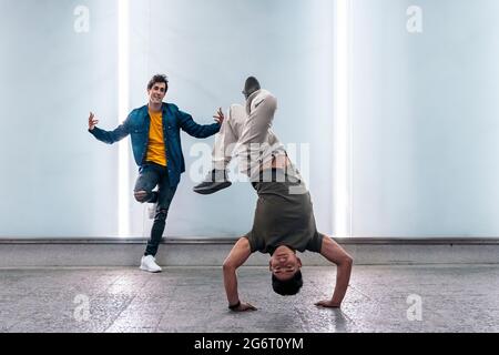 Amazing young men practicing break dance together against white wall with lights. Stock Photo