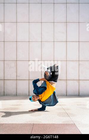 Cool dancer doing handstand in the street against white wall and looking at camera. Stock Photo
