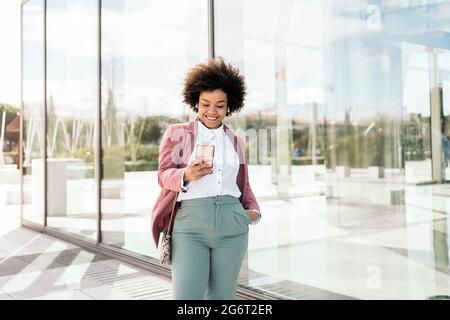 Happy black business woman using her mobile phone outdoors. She is wearing formal clothes and using earphones. Stock Photo