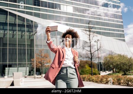 Happy black business woman with afro hair smiling and taking selfie with her mobile phone. Stock Photo