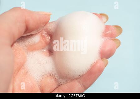 Female hand with white soapy foam on a blue background. Stock Photo