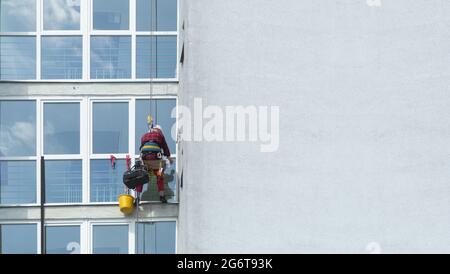 A man washes windows in a multi-storey building. Professional window cleaning. A climber washes a window on a skyscraper, bottom view. Background with Stock Photo