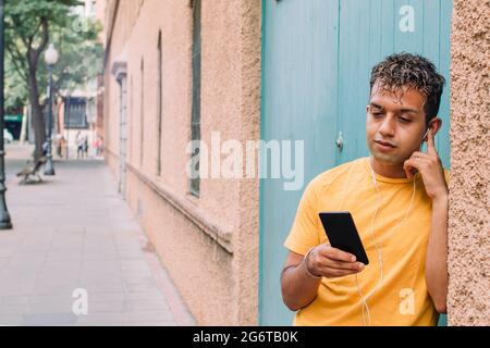 Young latino man listening music on cell phone on street background with copyspace Stock Photo