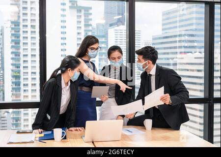 Multiethnic business team meeting and discussing with business plan in new normal office. Colleagues wearing face mask protective pandemic of Coronavi Stock Photo