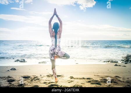 woman in sport clothes practicing yoga and meditating on beach in morning Stock Photo