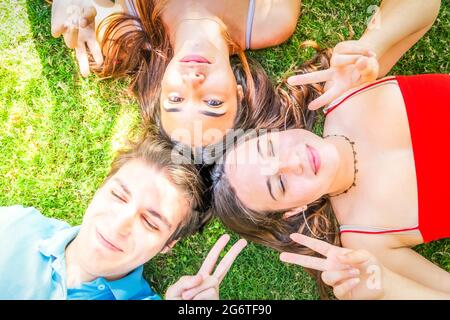 Group of happy teenagers friends relaxing on green grass in meadow and showing peace sign Stock Photo