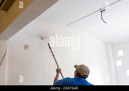 Worker painting wall with coat of paint using paint roller Stock Photo