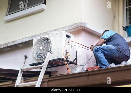 Technician installing outdoor air conditioner compressor unit on wall Stock Photo