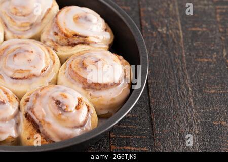 Frosted Cinnamon Rolls in a Pan on a Rustic Wooden Table Stock Photo