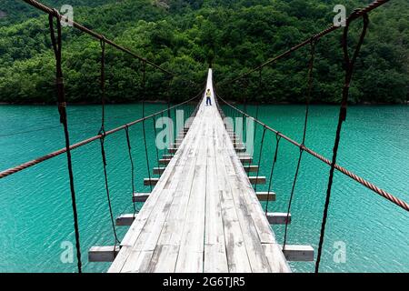 Woman walking on hanging or suspension bridge over beautiful emerald river, Albania Stock Photo