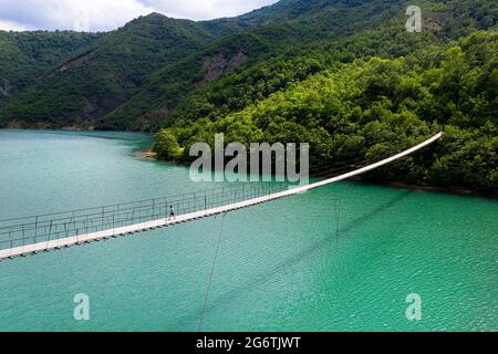 Boy walking on hanging or suspension bridge over beautiful emerald river, Albania Stock Photo