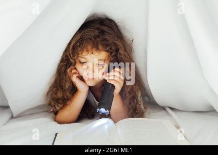 Little girl reads a book with a flashlight in bed Stock Photo