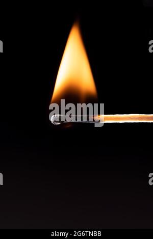 Triangular flame of fire on a match over a black background. Burning match on a black background with space for text. Stock Photo