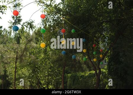 Plastic multicolored balls hang on a rope against a tree background Stock Photo