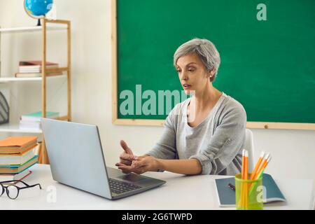 Online learning education. Female senior teacher is teaching students or schoolchildren using a video conference has a laptop in the classroom. Stock Photo