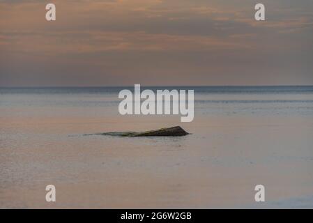 sunset in the sea with clouds and calm water on the surface of which sunlight reflects by creating a light path Stock Photo