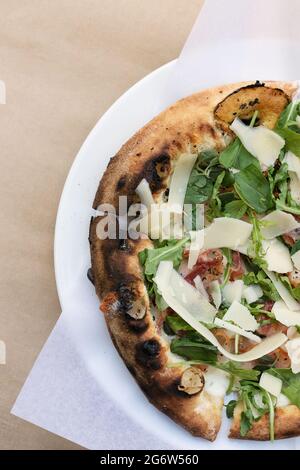 close-up Italian pizza with bacon, arugula, parmesan, mozzarella, basil and oregano on a white plate. Beige background Stock Photo