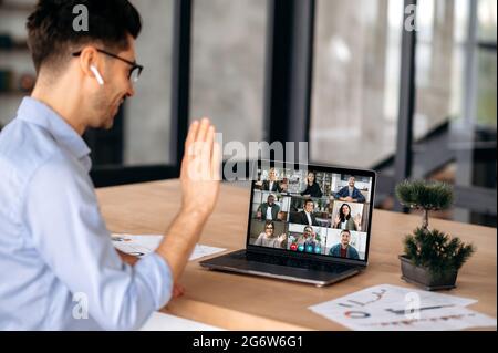 Caucasian successful businessman having virtual online meeting with diverse people, talking with multiracial colleagues via video conference call using laptop, sits in office, greeting interlocutors Stock Photo