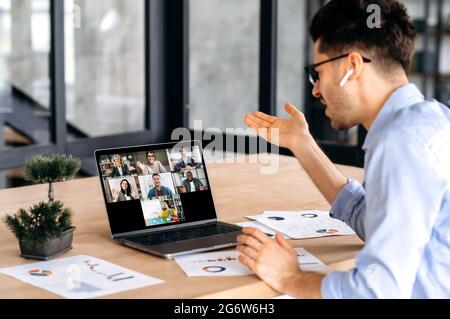 Online education, e-learning concept. Smart caucasian guy gains knowledge watching lesson online and learning distantly. Young man listening lecture from female teacher on video call using laptop Stock Photo