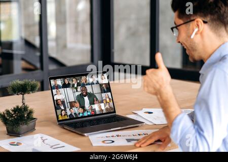 Brainstorm, video briefing. Caucasian man having online virtual meeting via video conference with successful multiracial coworkers, using laptop, sits in office, planning marketing strategy and ideas Stock Photo