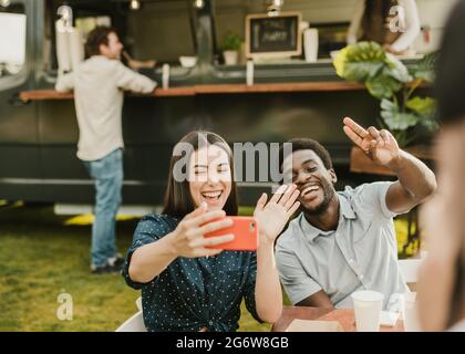 Multiracial friends having fun doing selfie eating at food truck outdoor - Focus on african man face Stock Photo