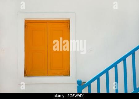 Yellow window shutters on whitewashed house with blue stair railing on the Greek island of Mykonos Stock Photo