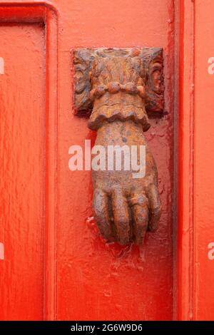 Rusted metal door knocker in the shape of a hand on a red door in the Mykonos town of Chora in the Greek Islands Stock Photo