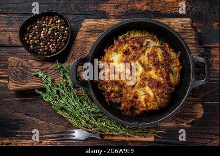 Fried Potato pancakes or Fritters with herbs in a pan. Dark wooden background. Top view Stock Photo