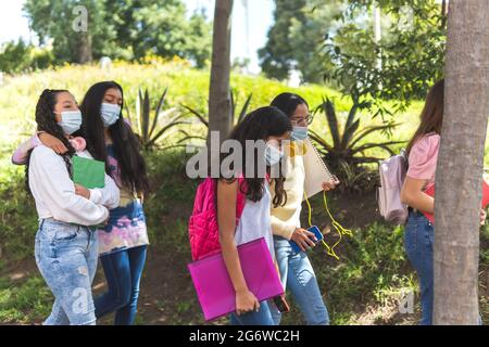 A group of Latina adolescent women with a mask for prevention of covid 19 walk with their notebooks and backpacks down the street towards high school Stock Photo