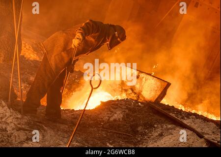 The process of releasing pig iron from a blast furnace. A man works with molten metal Stock Photo