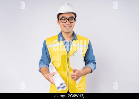 Smiling young asian civil engineer wearing helmet hard hat standing on isolated white background. Mechanic service concept. Stock Photo