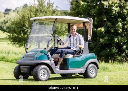 Portrait of smiling male golfer riding golf cart showing thumbup sign Stock Photo