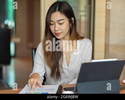 Portrait of businesswoman looking on financial paper with tablet in office room Stock Photo