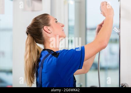 Side view of a skilled female worker checking a showerhead during quality control in the showroom of a modern sanitary ware shop Stock Photo