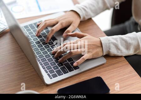 Close up of female fingers typing on laptop keyboard with mobile phone and financial papers on the wooden desk Stock Photo