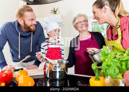 Happy mom, dad, granny and grandson together in kitchen preparing food Stock Photo