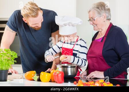 Mom, dad, granny and grandson together in kitchen preparing food Stock Photo