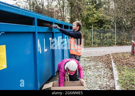 Woman and man putting waste paper in container at recycling center together Stock Photo