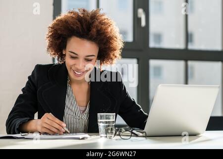 Portrait of African American female expert analyzing printed business report while sitting at desk in the office Stock Photo