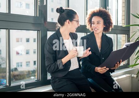 Two young female colleagues reviewing business reports during break in the office Stock Photo