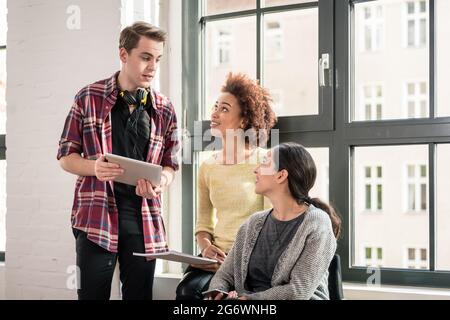 Three young employees using modern devices with wireless connection to internet during break in the office Stock Photo