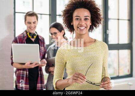 Portrait of young cheerful employee holding eyeglasses while looking at camera in the office Stock Photo