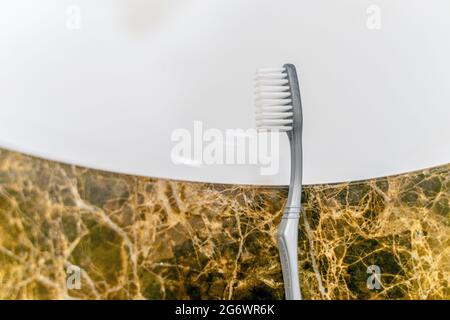 Toothbrush head lying on the edge of a white sink set on a marble stand. Stock Photo