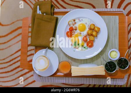 Fried eggs with ham and tomatoes, cappuccino, juice, jams, butter served on a tray as continental breakfast in hotel. Stock Photo