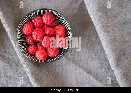 Red loganberries in the bowl on the gray background, summer berries Stock Photo