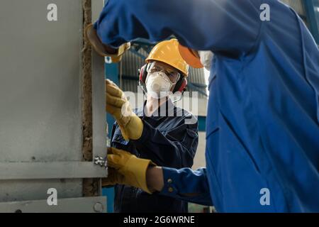 Two blue-collar workers wearing protective equipment while insulating an industrial pressure vessel Stock Photo