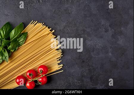 Spaghetti Italian pasta with basil leaves and tomatoes on dark textured background, arranged in the colors of the Italian flag. Top view. Copy space Stock Photo