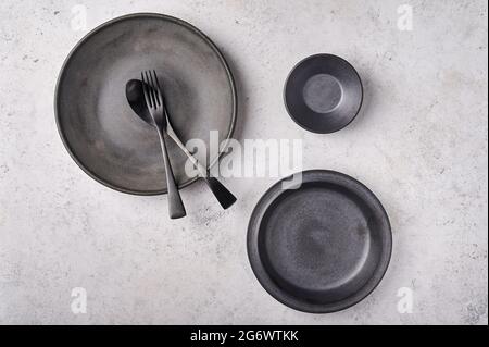 Empty plates, gravy boat, spoon and fork. Dark kitchen utensils set on light gray table. Top view flat lay with copy space Stock Photo